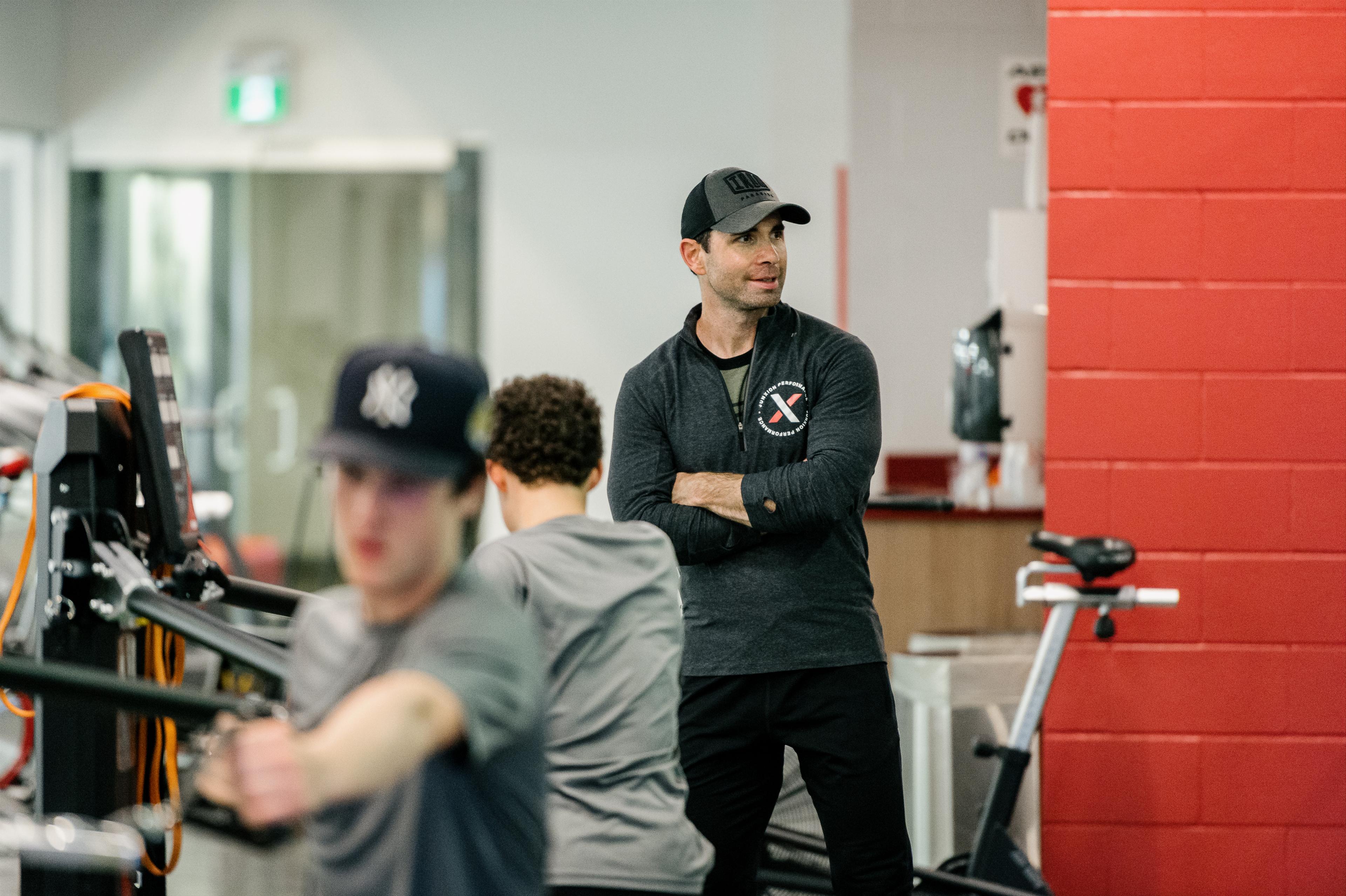 Andy O'Brien standing with his arms crossed overlooking athletes training at Junxion Performance