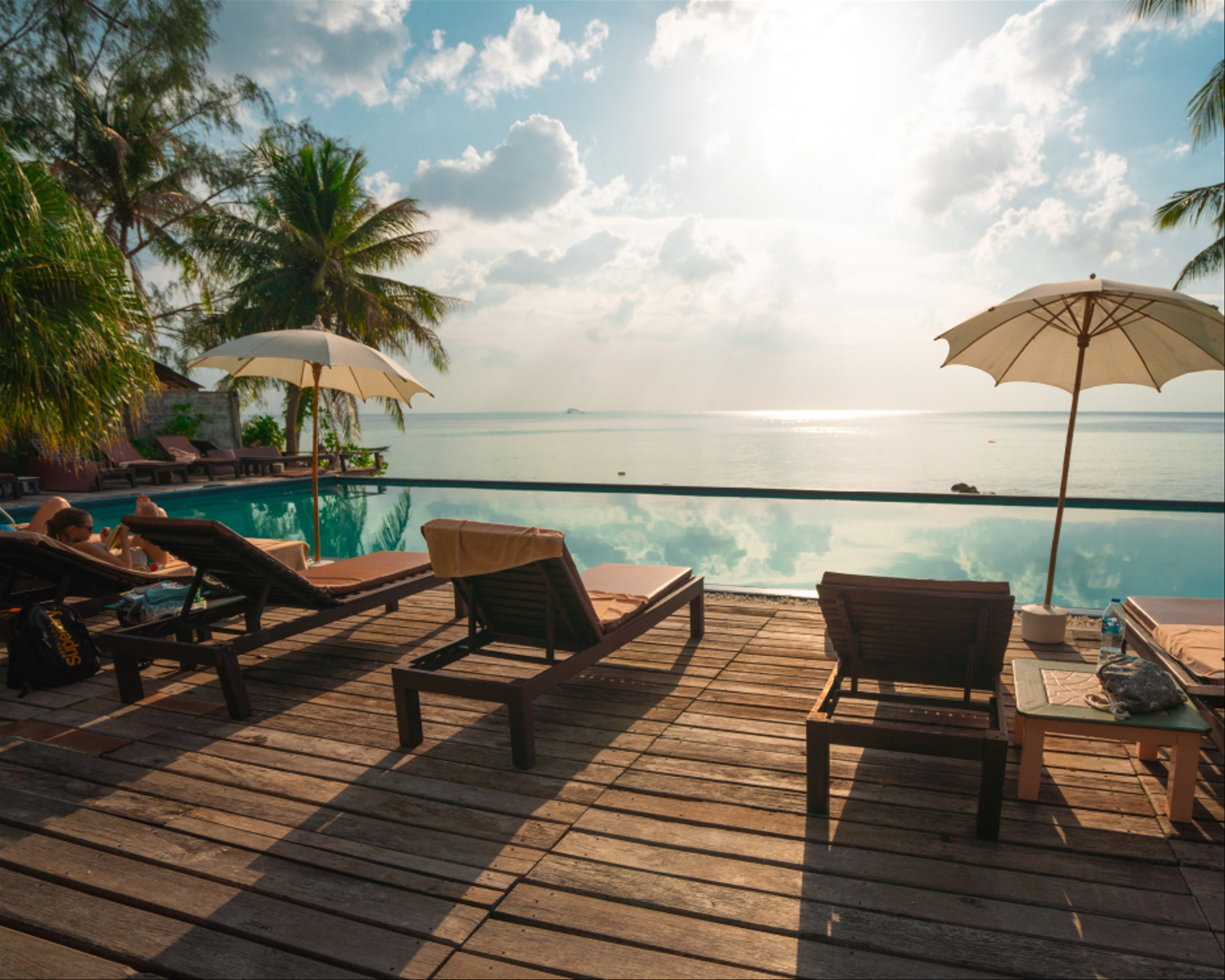 A row of reclining beach chairs on a deck overlooking a beautiful ocean and a sunny sky.